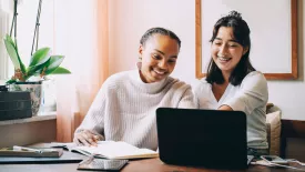 Two women smiling while looking at laptop