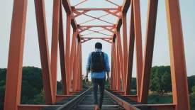 Person with backpack walking across an orange metal bridge