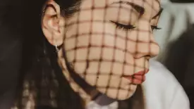Close-up of woman's face covered by a chain-link shadow