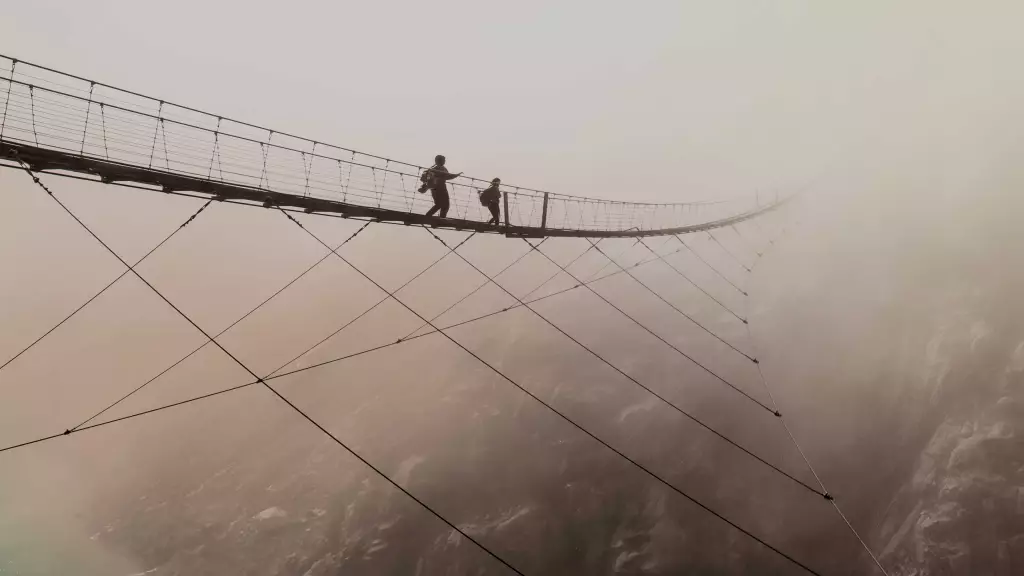 Wide shot of two people walking across suspended bridge high in the clouds