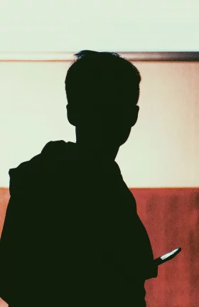 Silhouette a Young Adult Holding a Phone with Brown Wall
