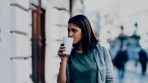 Woman in sweater walking outside and drinking coffee