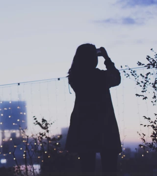 Woman in a coat outside at dusk taking photo of sunset