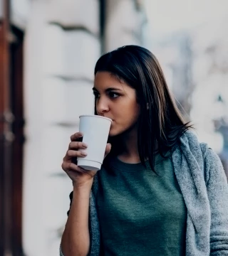 Woman in sweater walking outside and drinking coffee
