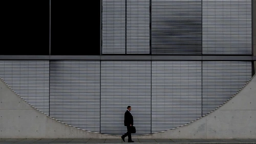 Side view of man with briefcase walking in front of concrete building