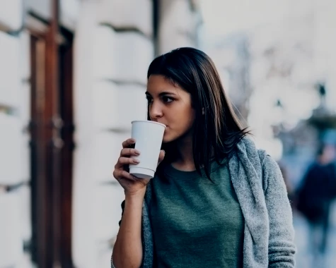Woman in sweater walking outside and drinking coffee