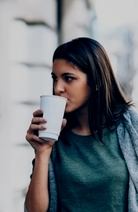 Woman in sweater walking outside and drinking coffee