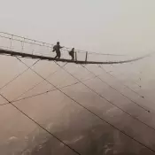 Wide shot of two people walking across suspended bridge high in the clouds