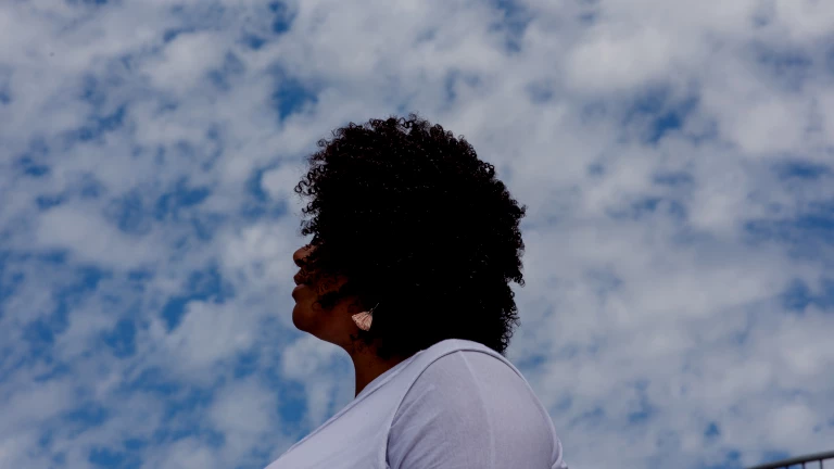 Side profile of a Black woman standing against a blue sky