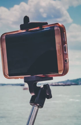 Close-up of smartphone attached to selfie stick pointed at a body of water