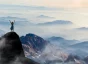 Person standing on a far-away mountain top with their arms in the air