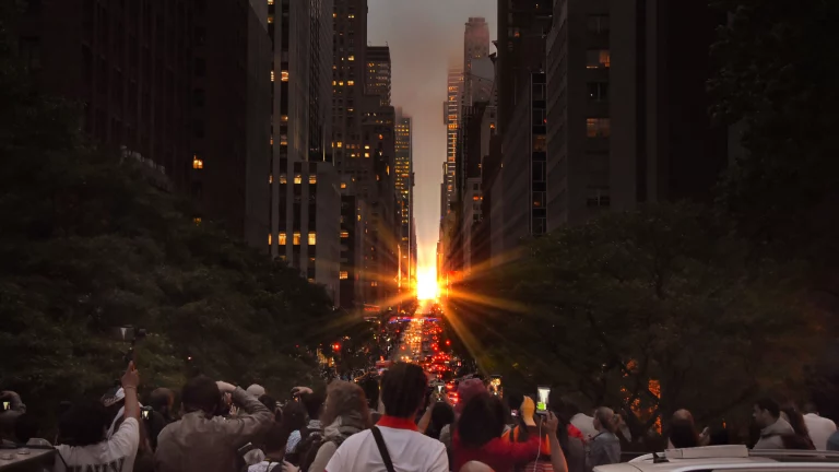 A crowd of people staring at the sunset between two city buildings