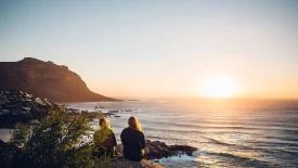 Rear view of female friends sitting at beach against clear sky during sunset
