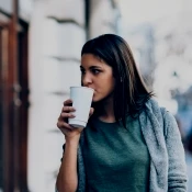 Woman in sweater walking outside and drinking coffee
