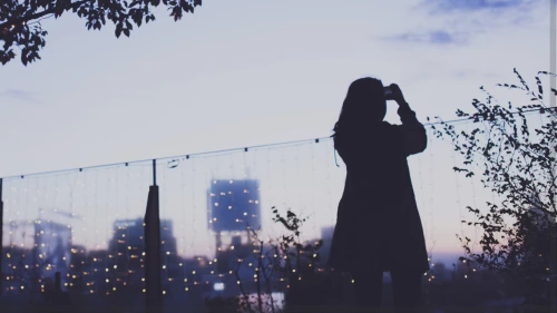 Woman in a coat outside at dusk taking photo of sunset