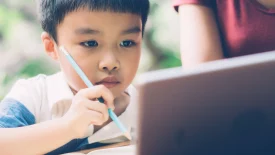 A young boy holding a pencil while looking at a screen