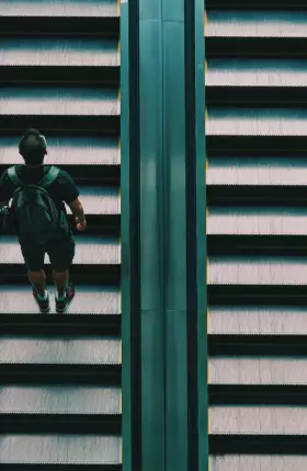 Man with backpack climbing an escalator