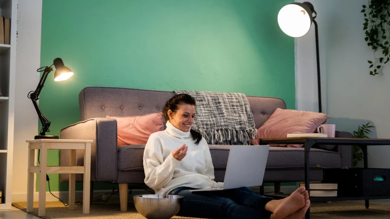 television business model Young woman sitting on living room floor eating snacks and using her laptop