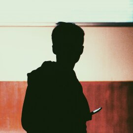 Silhouette a Young Adult Holding a Phone with Brown Wall