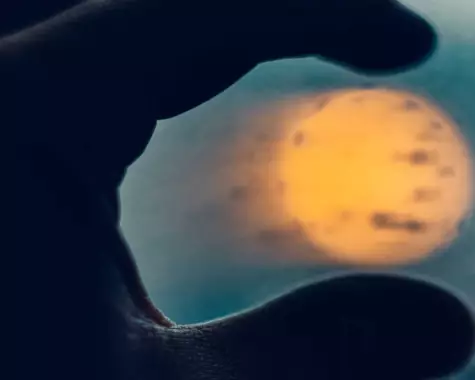 Close-up of person's hand holding sun between fingertips