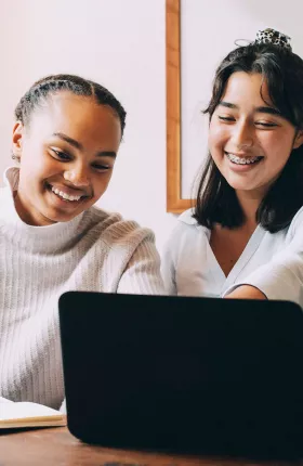 Two women smiling while looking at laptop
