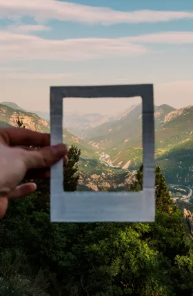 Person holding empty white picture frame in front of a mountainside
