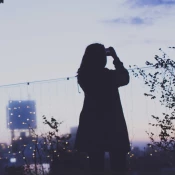 Woman in a coat outside at dusk taking photo of sunset