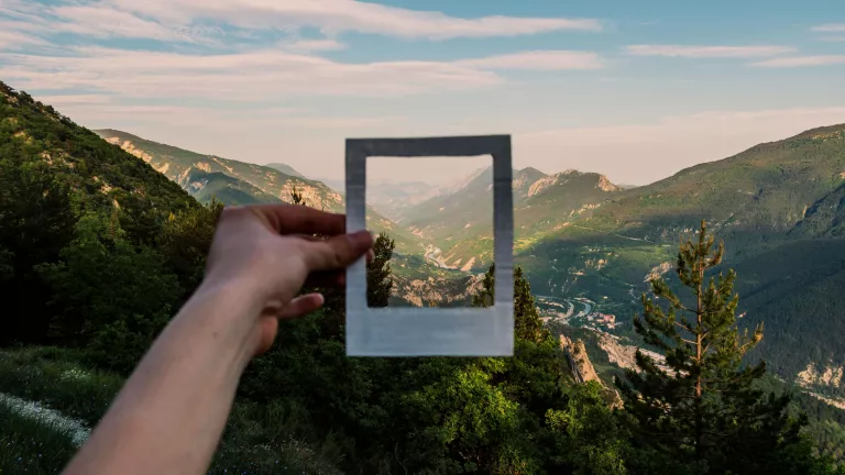 Person holding empty white picture frame in front of a mountainside