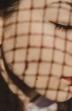 Close-up of woman's face covered by a chain-link shadow