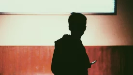 Silhouette a Young Adult Holding a Phone with Brown Wall