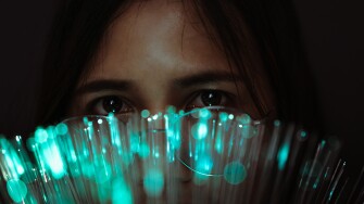 Woman holding blue fiber optic cables in front of her eyes