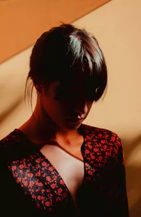 Woman with bangs posing against a brown wall looking down