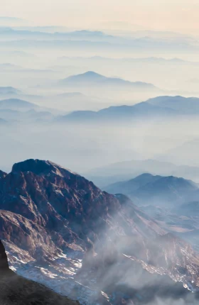Person standing on a far-away mountain top with their arms in the air