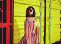 Woman in bright colors and red sunglasses posing against a yellow wall