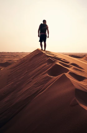 Person standing atop an orange sand dune