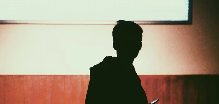 Silhouette a Young Adult Holding a Phone with Brown Wall