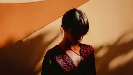 Woman with bangs posing against a brown wall looking down