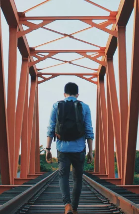 Person with backpack walking across an orange metal bridge